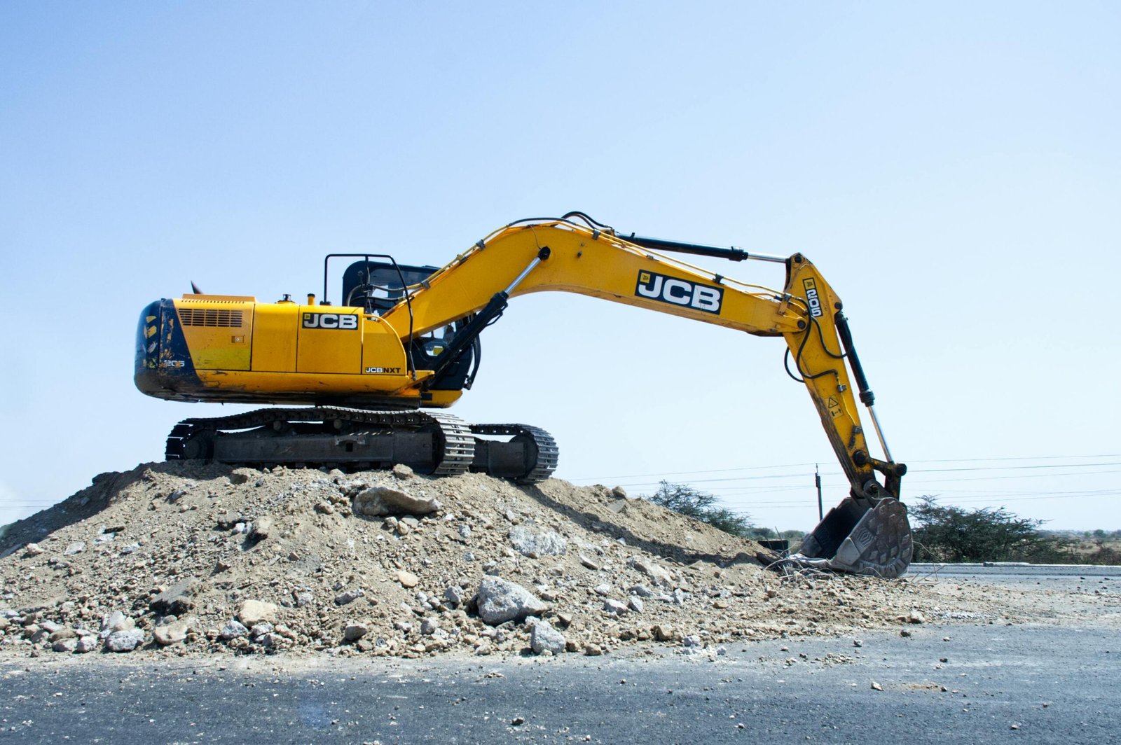 Services Yellow excavator on a pile of dirt at a construction site under clear blue sky.