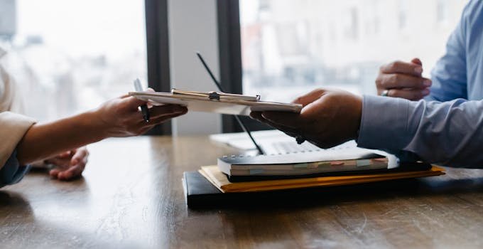 Services Crop anonymous ethnic woman passing clipboard to office worker with laptop during job interview